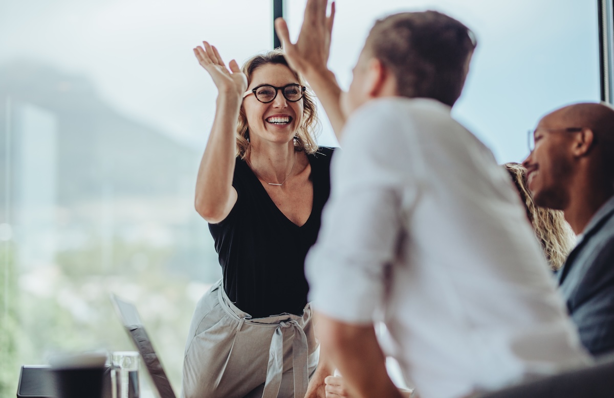 Team members in an office celebrate together with raised hands during a collaborative meeting.